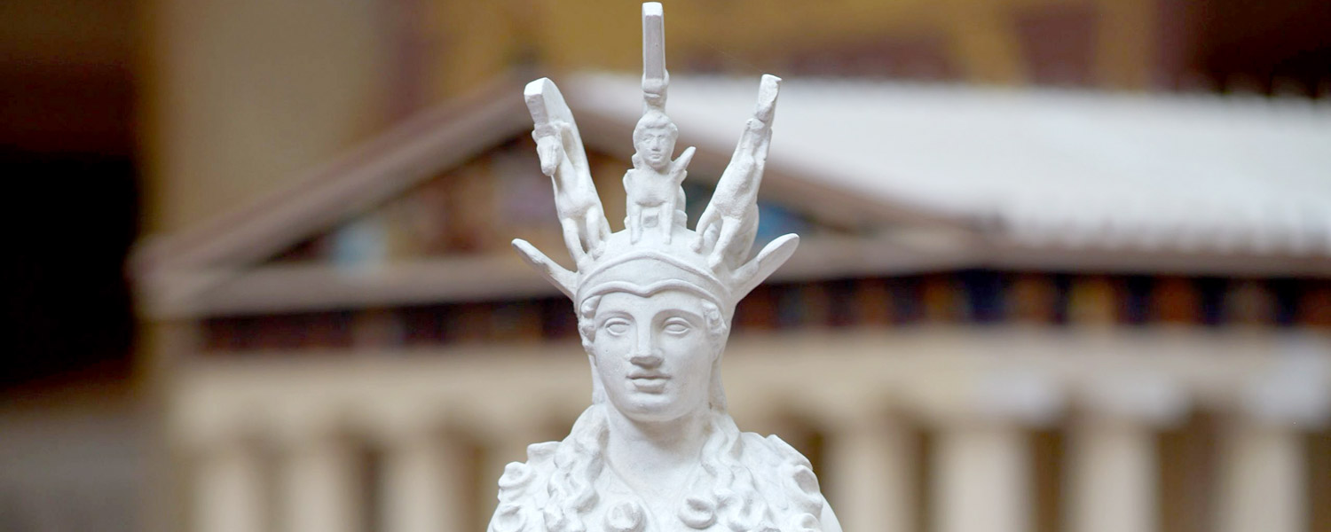 Das Bild zeigt eine Frau bis zu ihrer Brust. Es ist eine weiße Statue aus Gips. Die Frau hat einen Helm auf ihrem Kopf.