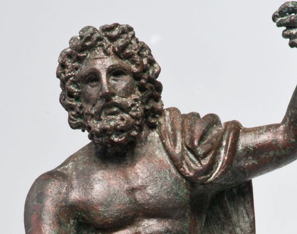 Ein Teil von einem Mann aus Bronze. Sein Oberkörper ist nackt. Der linke Arm ist gehoben. Auf seiner linken Schulter ist ein Tuch.